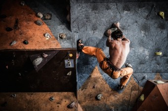 Muscular man practicing rock-climbing on a rock wall indoors