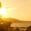 woman meditating in lotus pose on beach at sunset