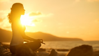 woman meditating in lotus pose on beach at sunset