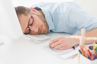 Young designer sleeping at his desk in creative office